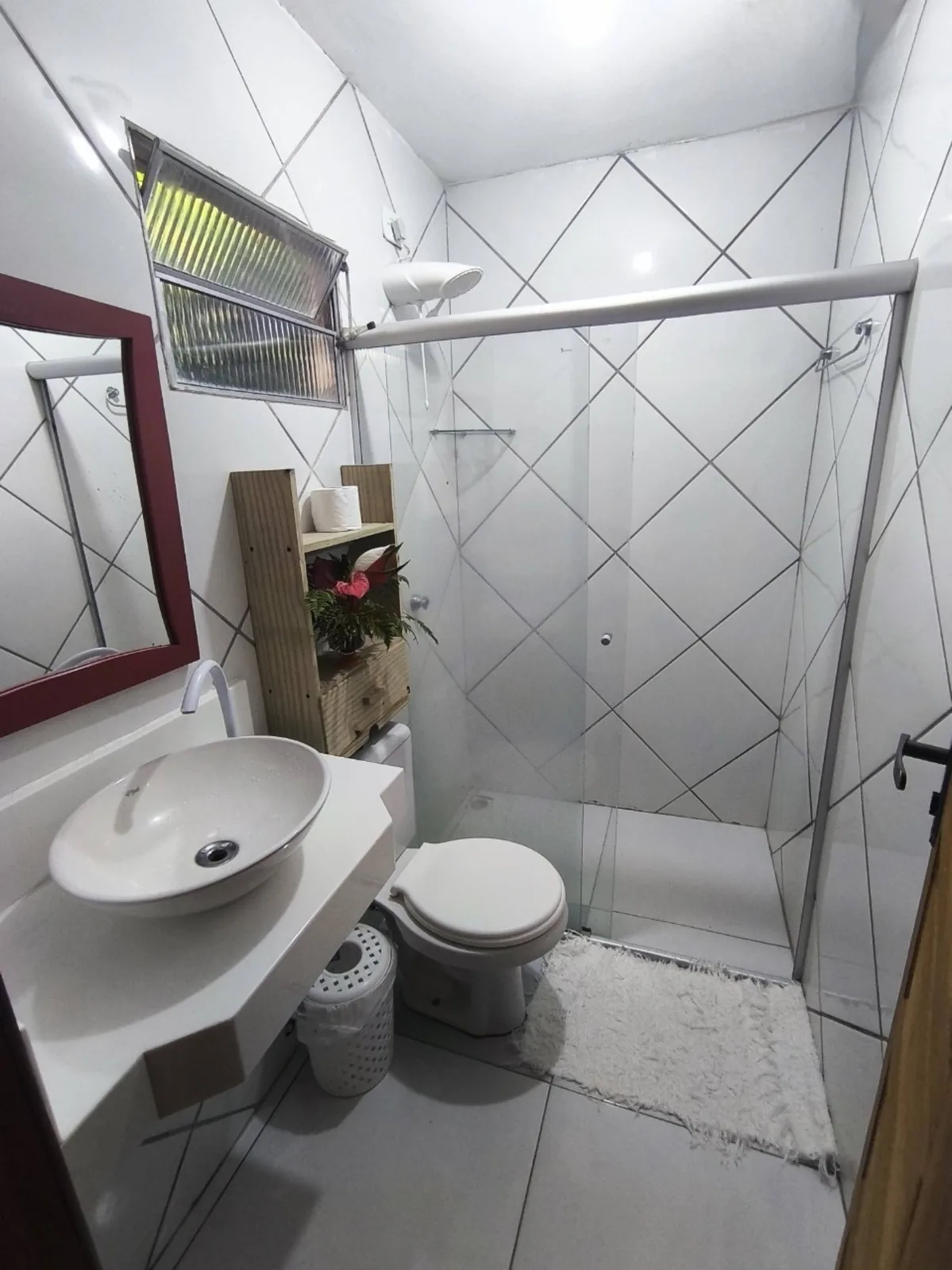 Banheiro da suíte da Casa da Lau em Trancoso com box de vidro, pia e espelho de moldura vermelha