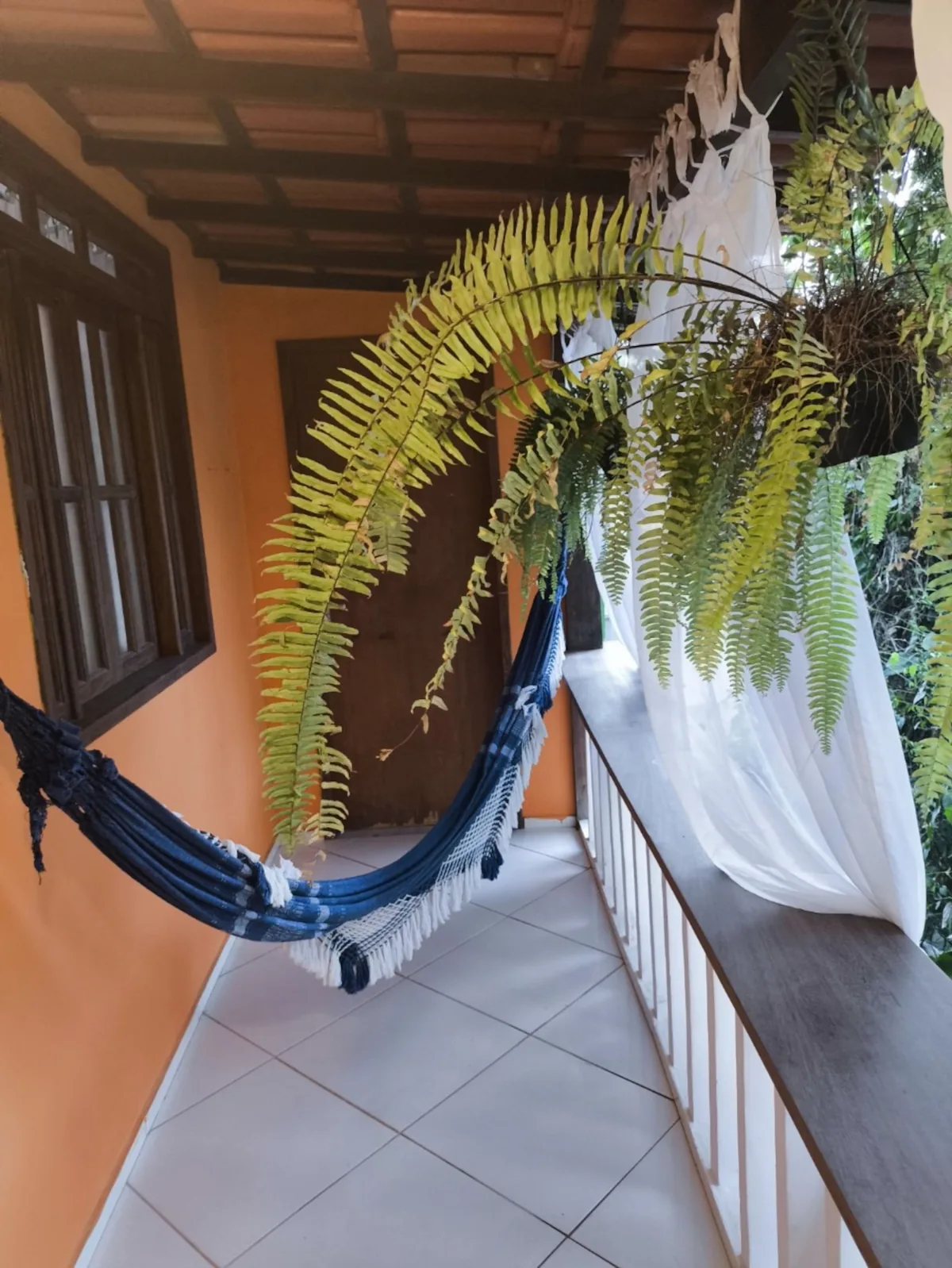 Varanda com rede de descanso e samambaias na casa de temporada em Trancoso, Bahia