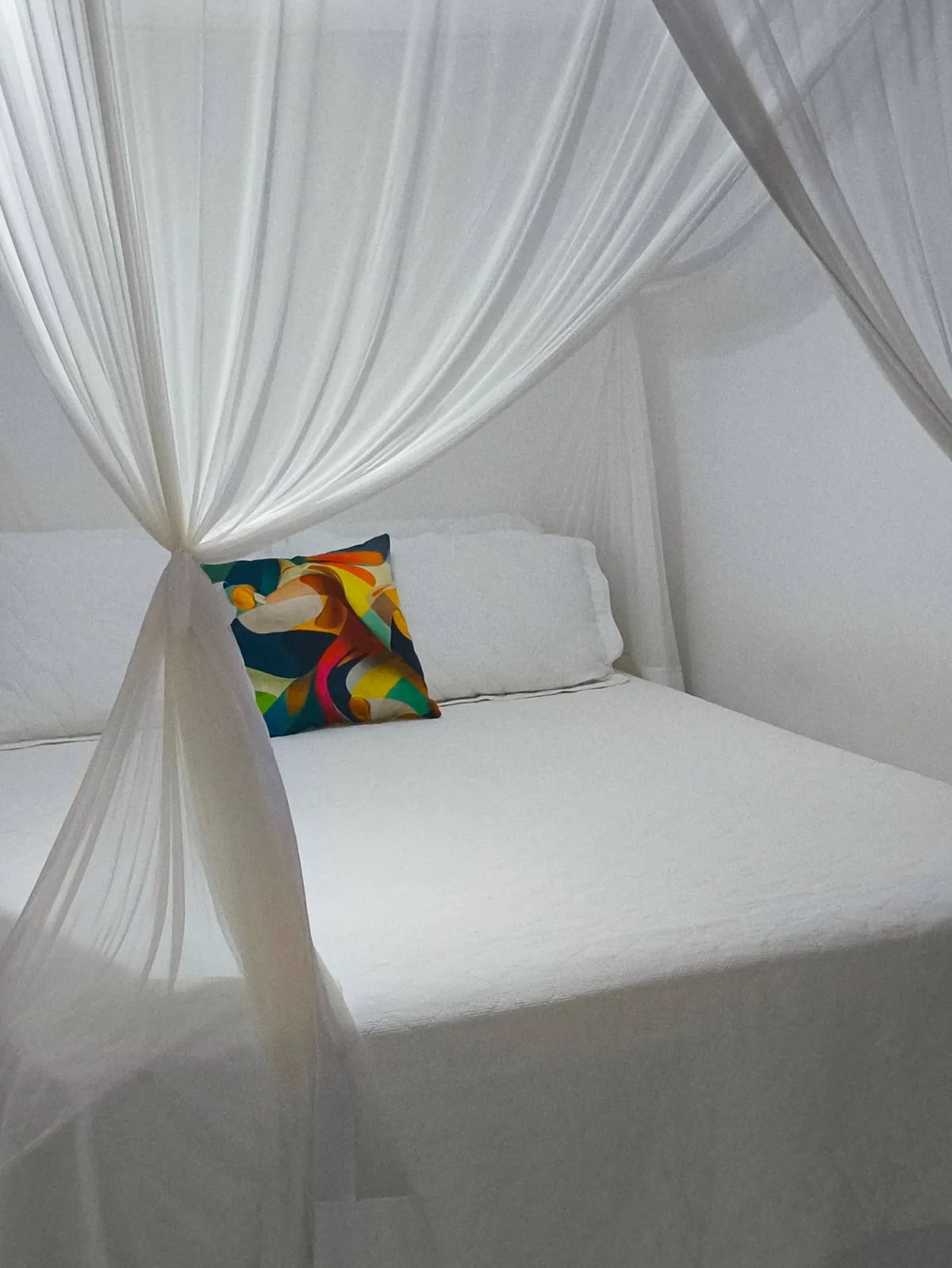 Detalhe da cama com dossel e almofada colorida na suíte da hospedagem em Trancoso BA