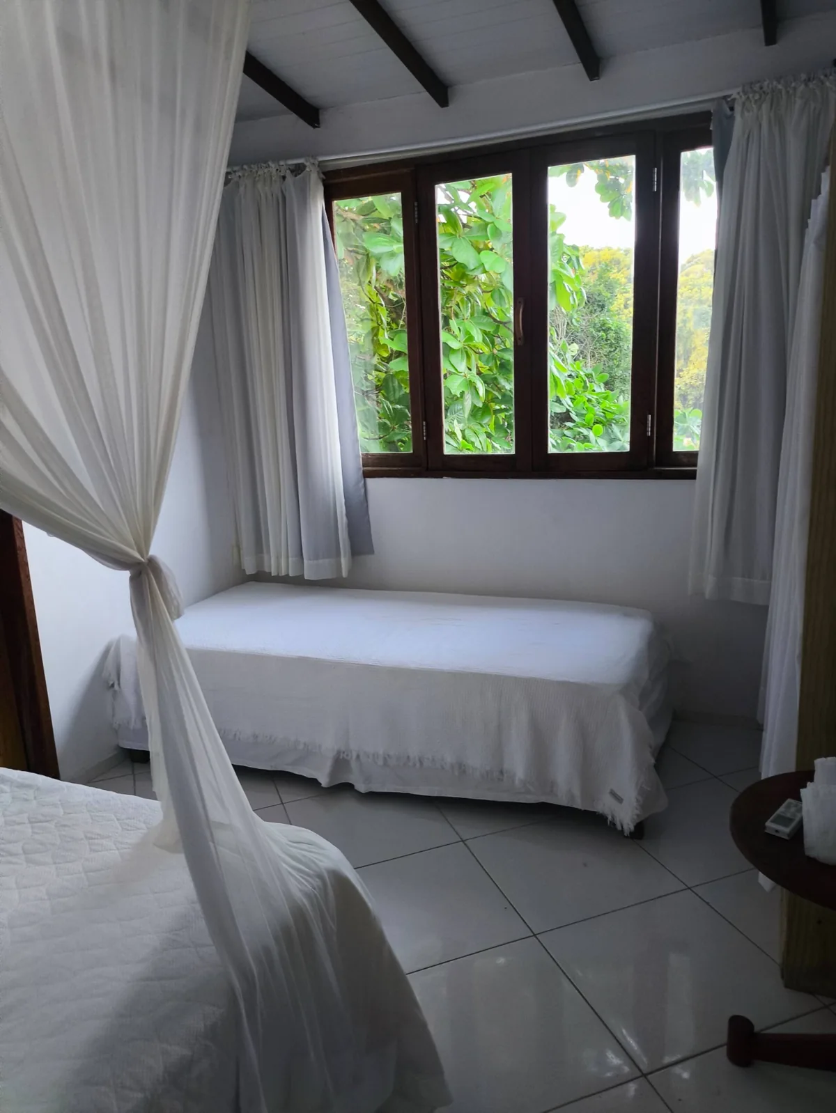 Quarto com cama de solteiro, dossel e janela com vista para o jardim em Trancoso BA